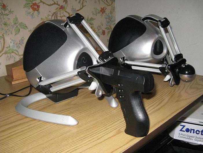 A Pair of black Novint Falcons sitting on a table, with the Pistol and Ball grip attachments