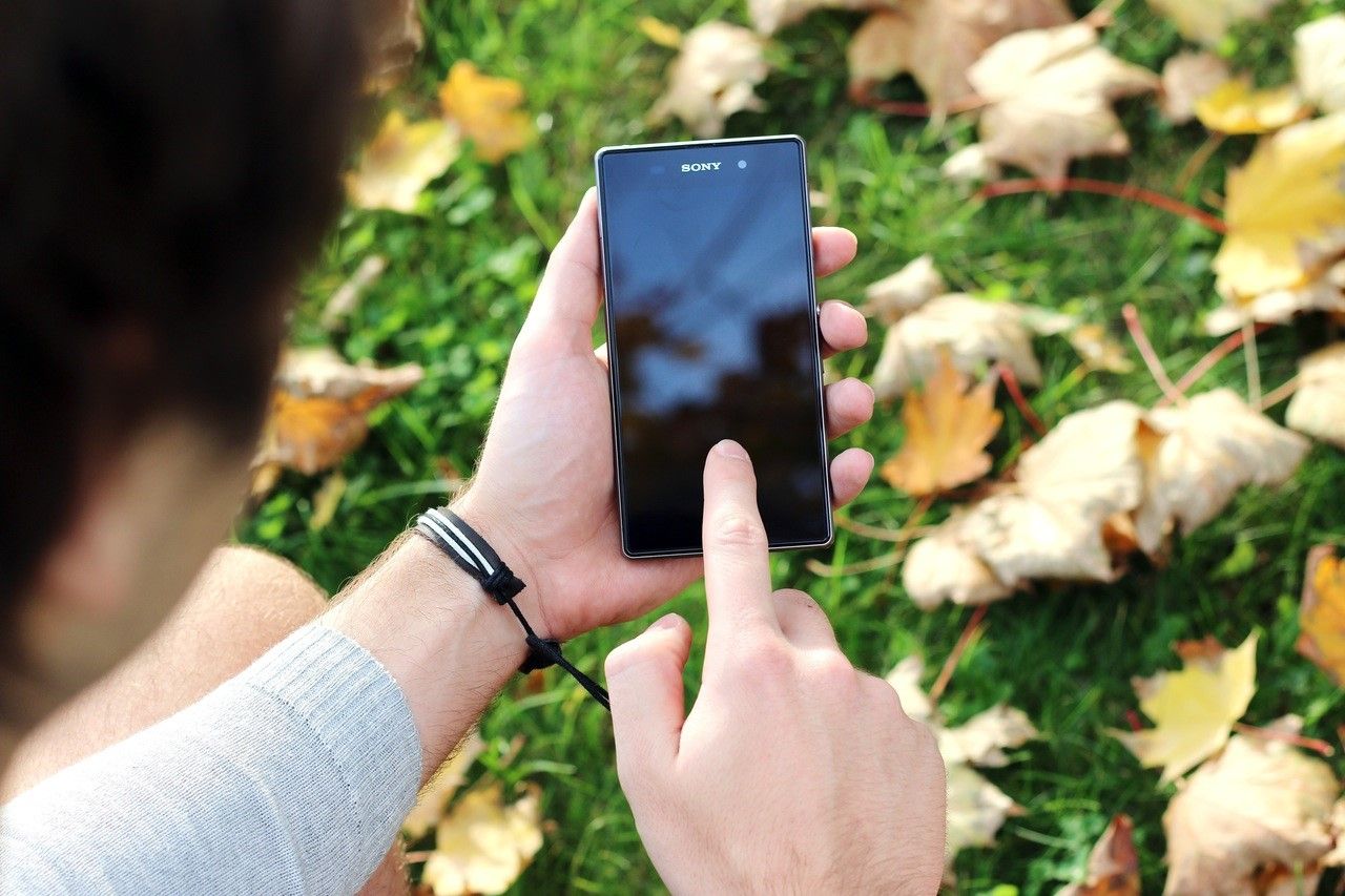 A person using a smartphone, pointing to the screen with the index finger.