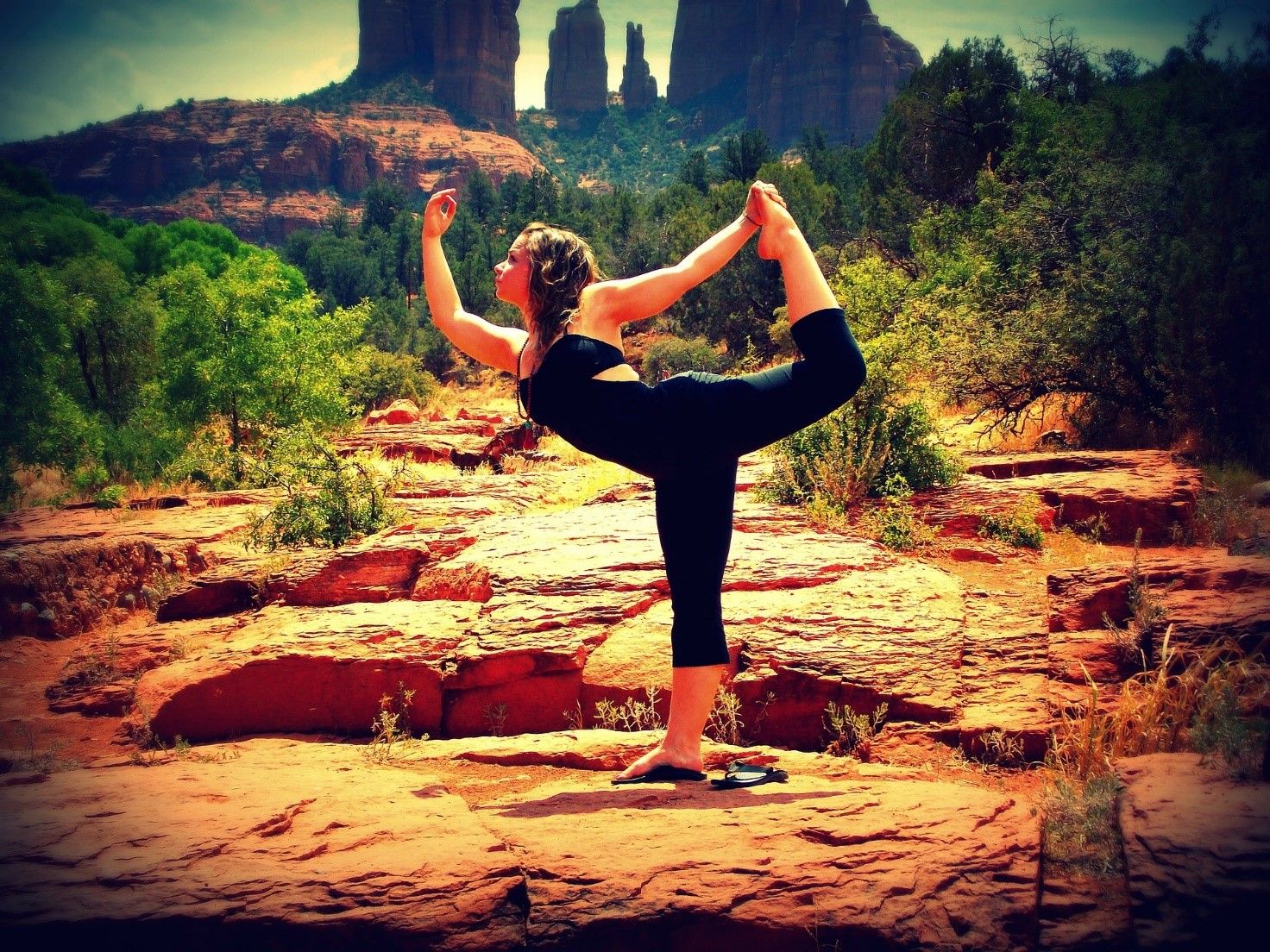 A woman standing on one leg, her other leg raised high up behind her. With one arm raised in front, she is holding the raised leg with the other arm.