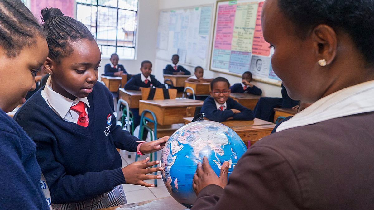 photo showing a classroom and two young students looking at a globe with their teacher