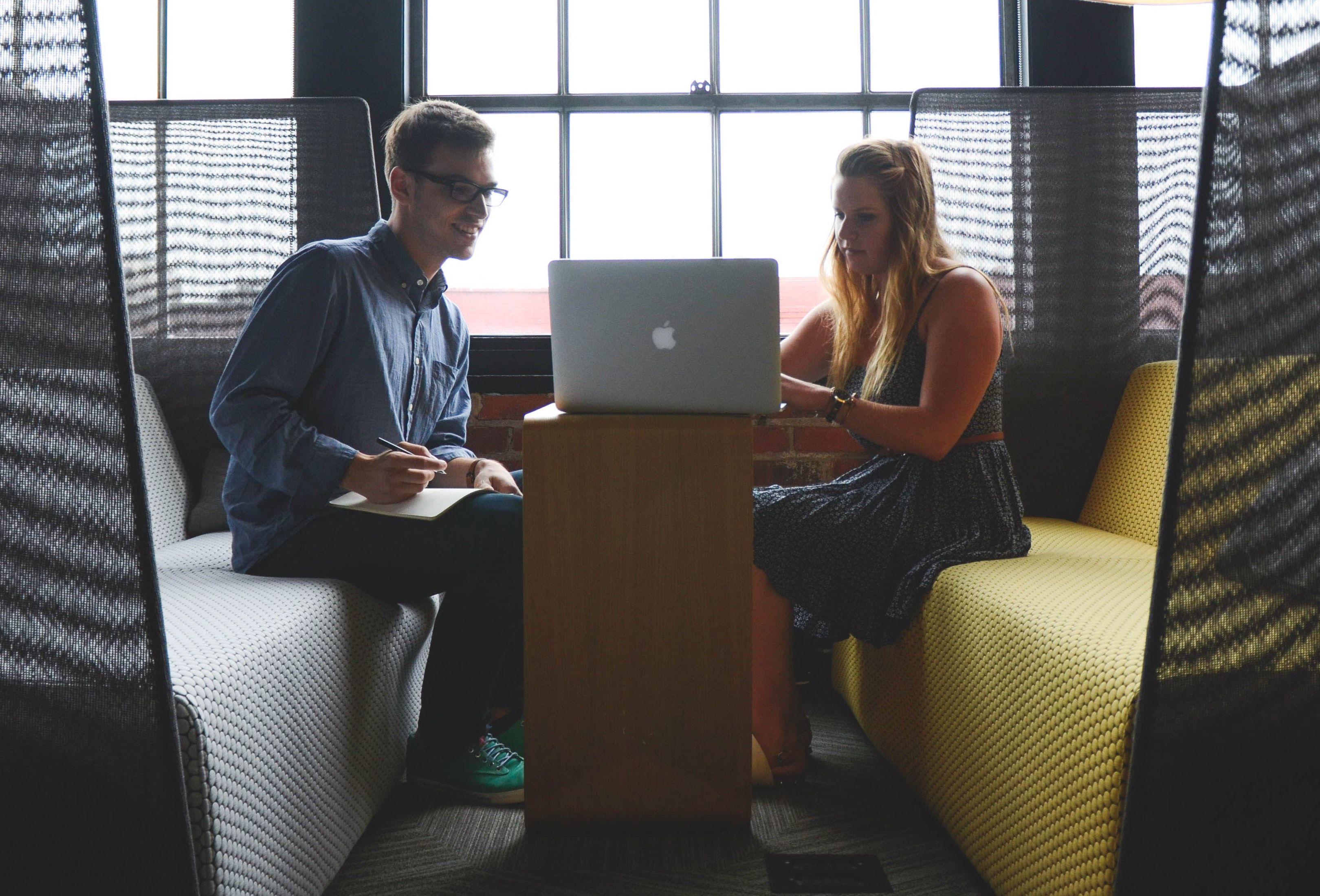 A woman works on a laptop as a man looks at the screen and takes notes.