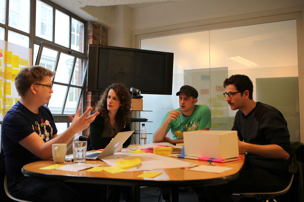 Four IDEO team members sitting around a table discussing a creative project.