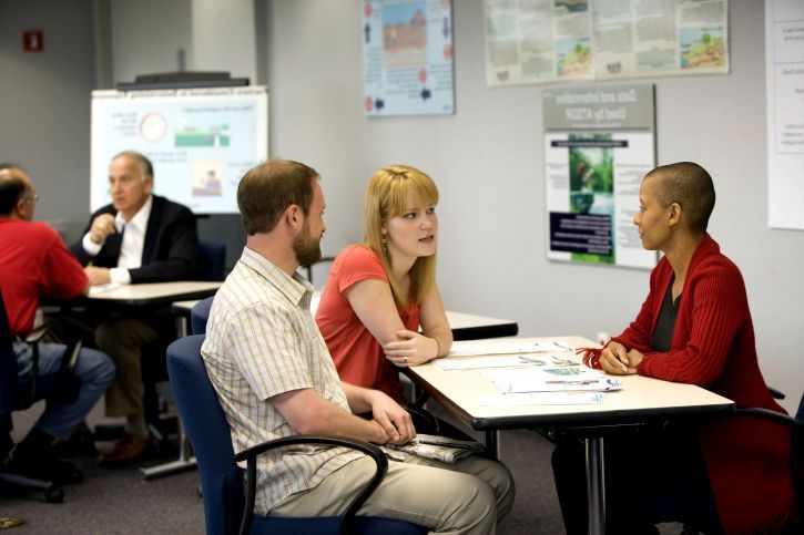 Photo of three people sitting at a large desk talking and collaborating.