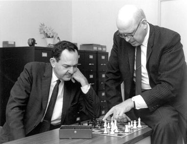 Black and white photo from the 1958 of Herbert Simon and Allen Newell playing chess while sitting at a desk.